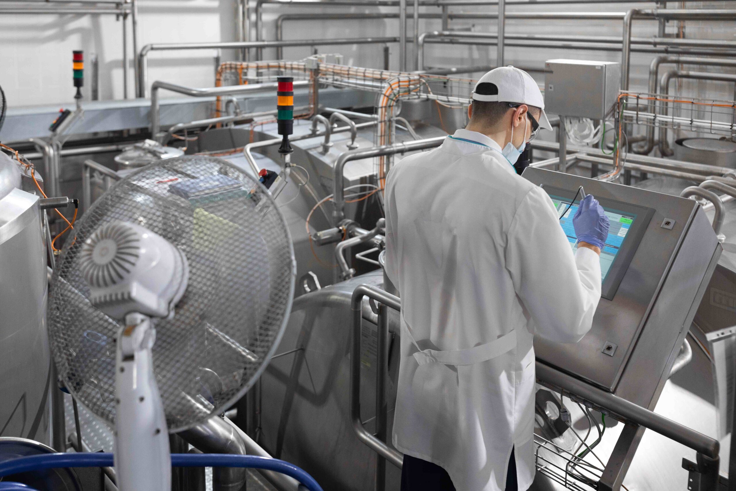 Inspector in a mask and a scrub stands with a folder-tablet in his hands at the dairy plant